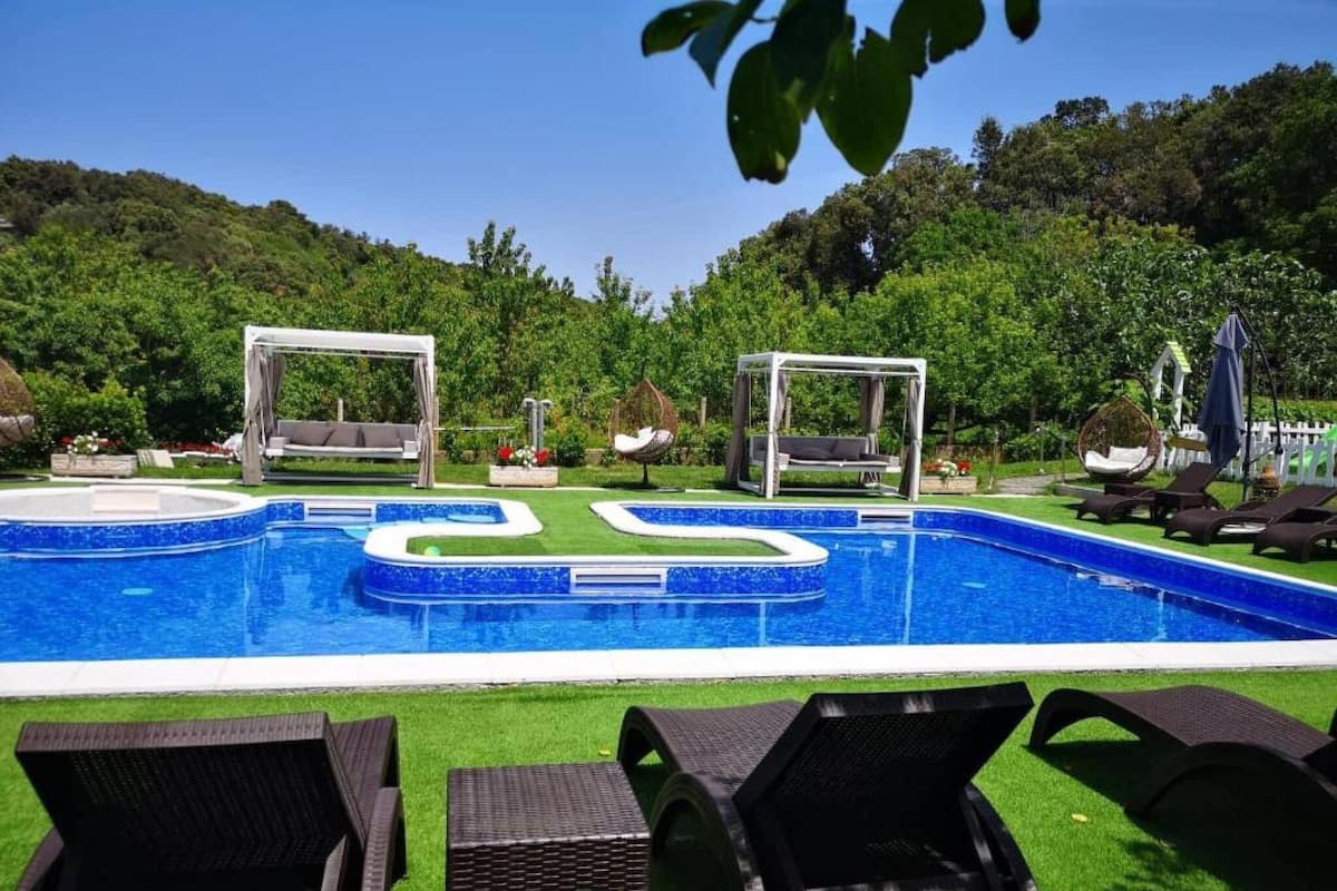 A swimming pool with two gazebos, lounge chairs, and a grassy area with trees in the background.