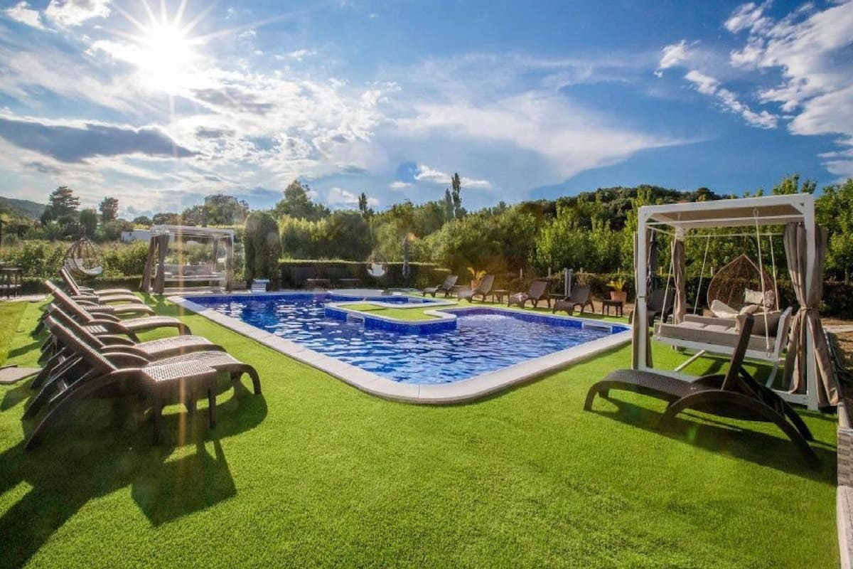 A pool area with a clear blue sky, surrounded by green artificial grass and lounge chairs.