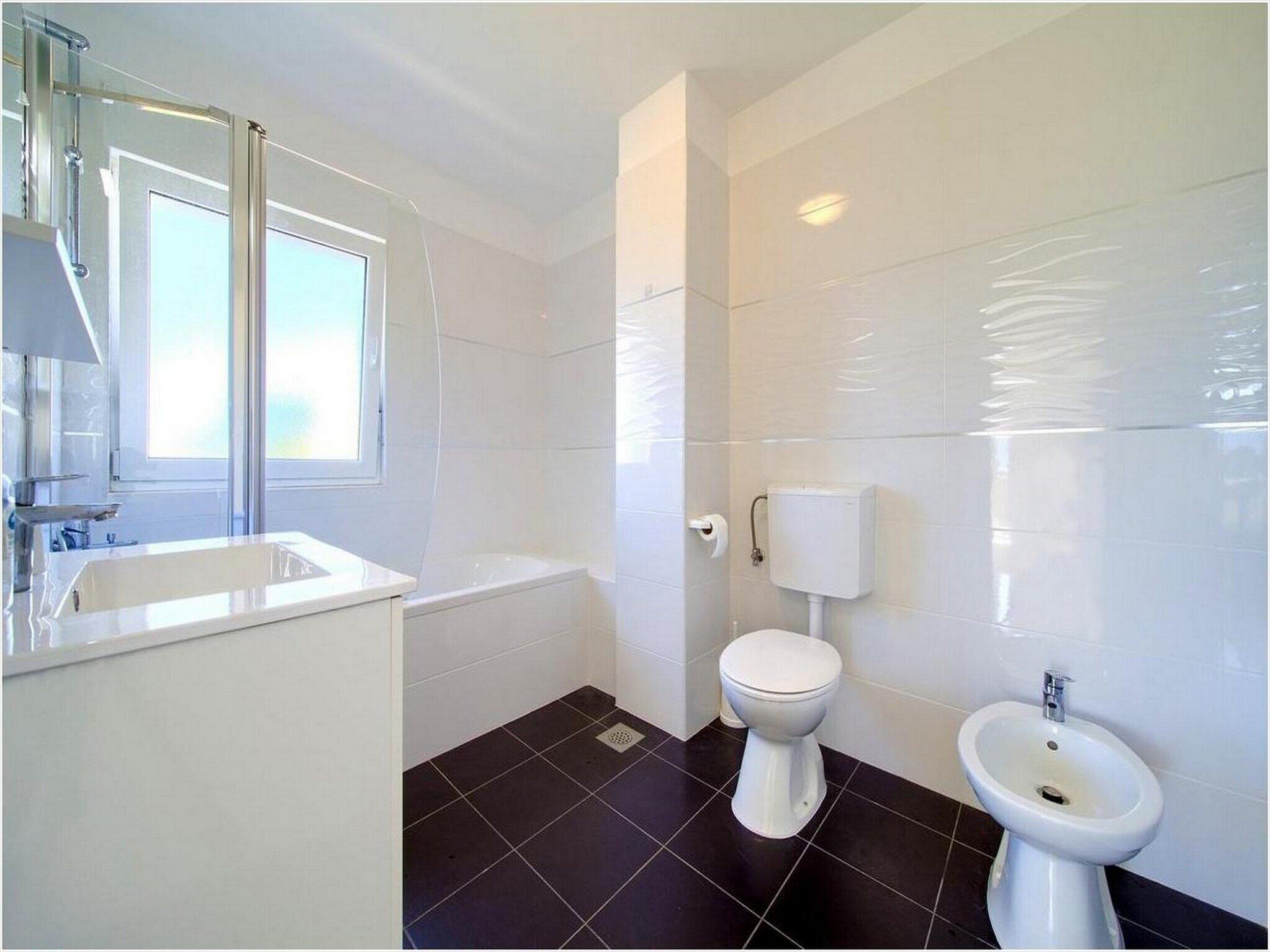 A bathroom with a bathtub, toilet, bidet, and a large mirror.
