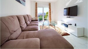 A modern living room with a sofa, a glass coffee table, a flat-screen TV, and a balcony with curtains. - Villa Isabella (Krk)