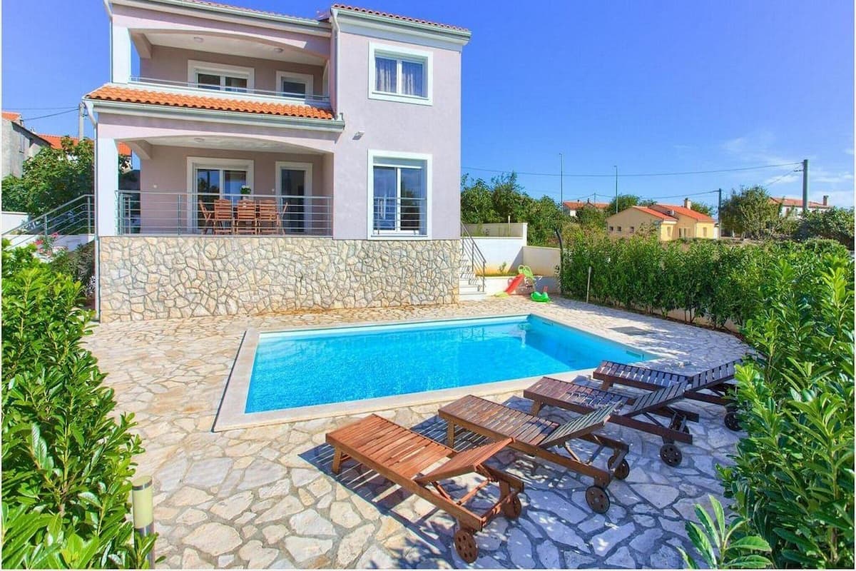 Ein zweistöckiges Haus mit Swimmingpool, Steinmauern und Gartenmöbeln.