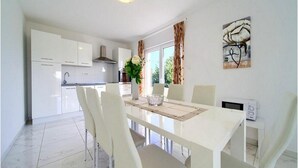 A modern kitchen with white cabinets, a central island, and a dining area with a white table and chairs. - Villa Isabella (Krk)