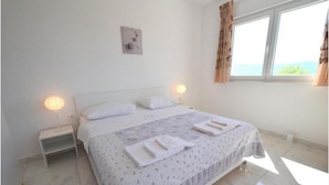 A neatly made bed with white linens and a patterned duvet, two bedside lamps, a small bedside table, and a window with curtains. - Villa Isabella (Krk)