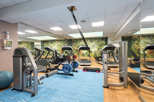 A gym with exercise equipment, mirrored walls, and a blue patterned floor.