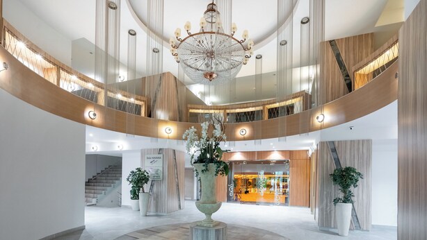 Tilava aula, jonka keskellä on suihkulähde, ja jossa on suuri kattokruunu sekä portaikko, joka johtaa ylemmälle tasolle.