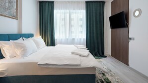 Hotellihuone, jossa on sänky, seinälle asennettu televisio ja ikkuna, jossa on verhot.