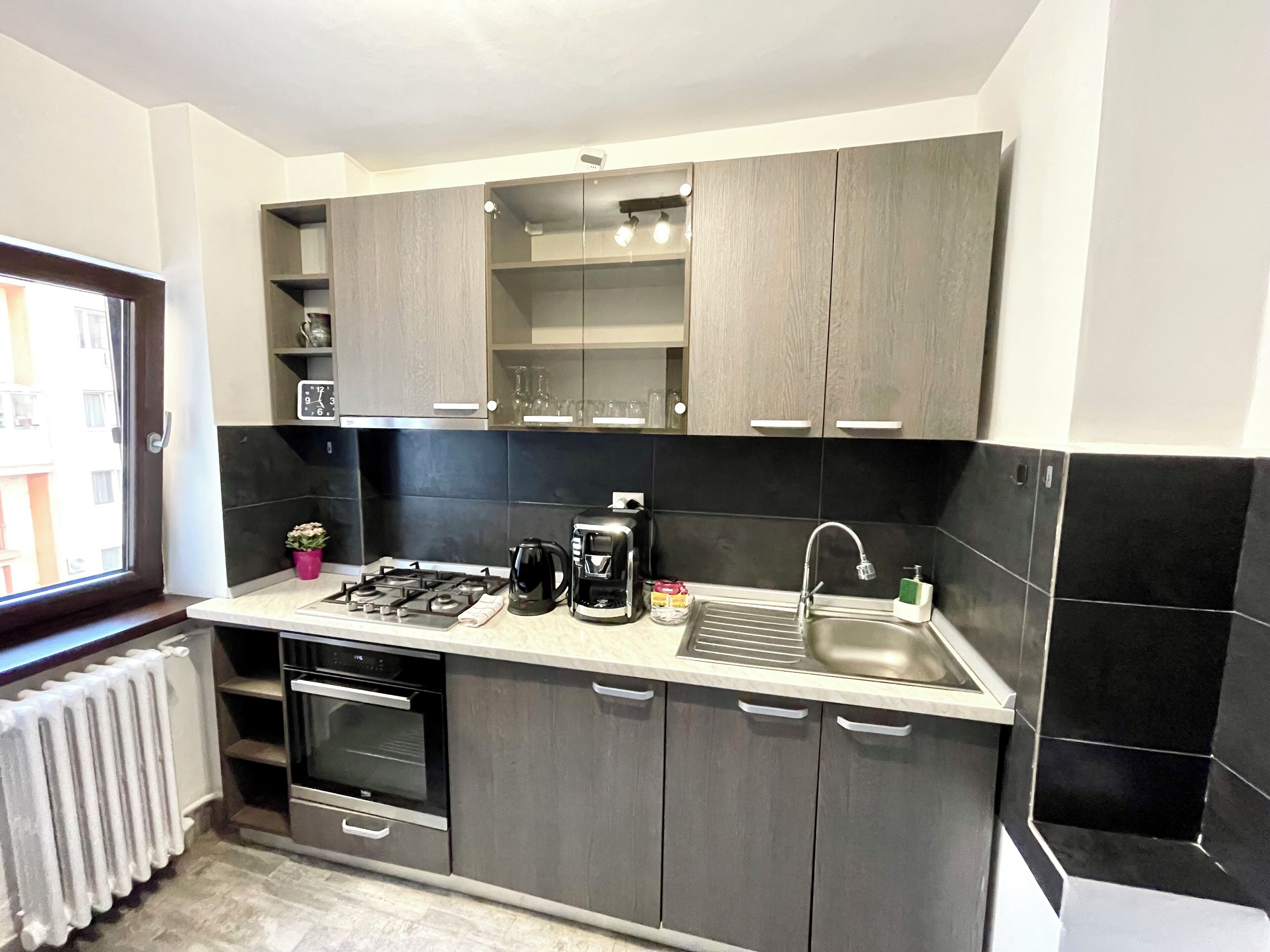A modern kitchen with dark cabinets, a gas stove, a coffee maker, and a sink.