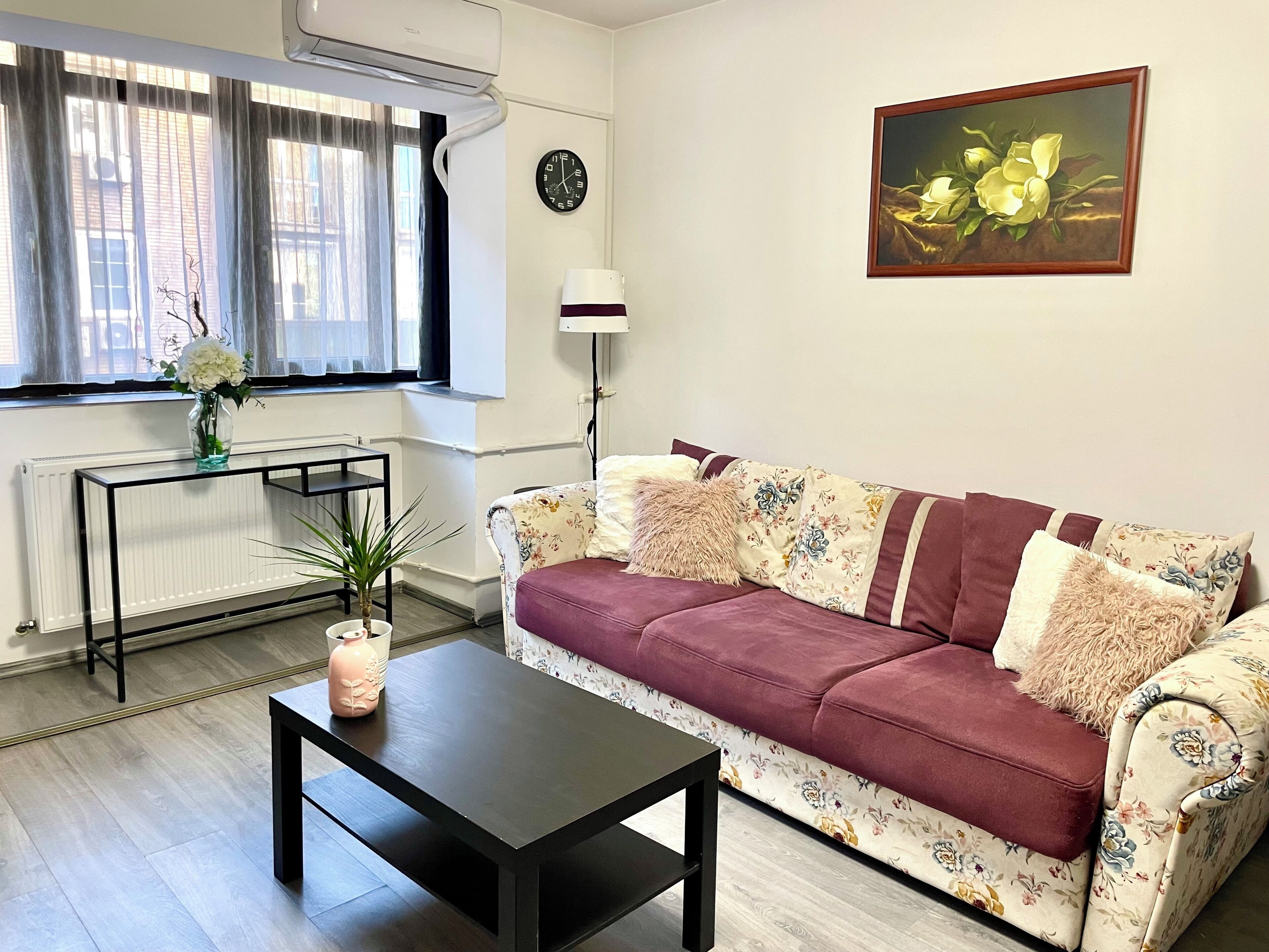 Un salón con un sofá, una mesa de centro, un radiador, un reloj y un cuadro en la pared.