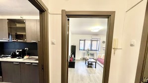 Una cocina moderna con armarios oscuros y una encimera, un área de estar con sofá y una mesita de centro, y un pasillo que conduce a otra habitación.