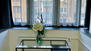 Una habitación con ventana, radiador y una mesa con un florero.