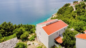 A coastal building with a red-tiled roof, surrounded by lush greenery and overlooking a calm sea with boats. - Villa Kosa (Brela)