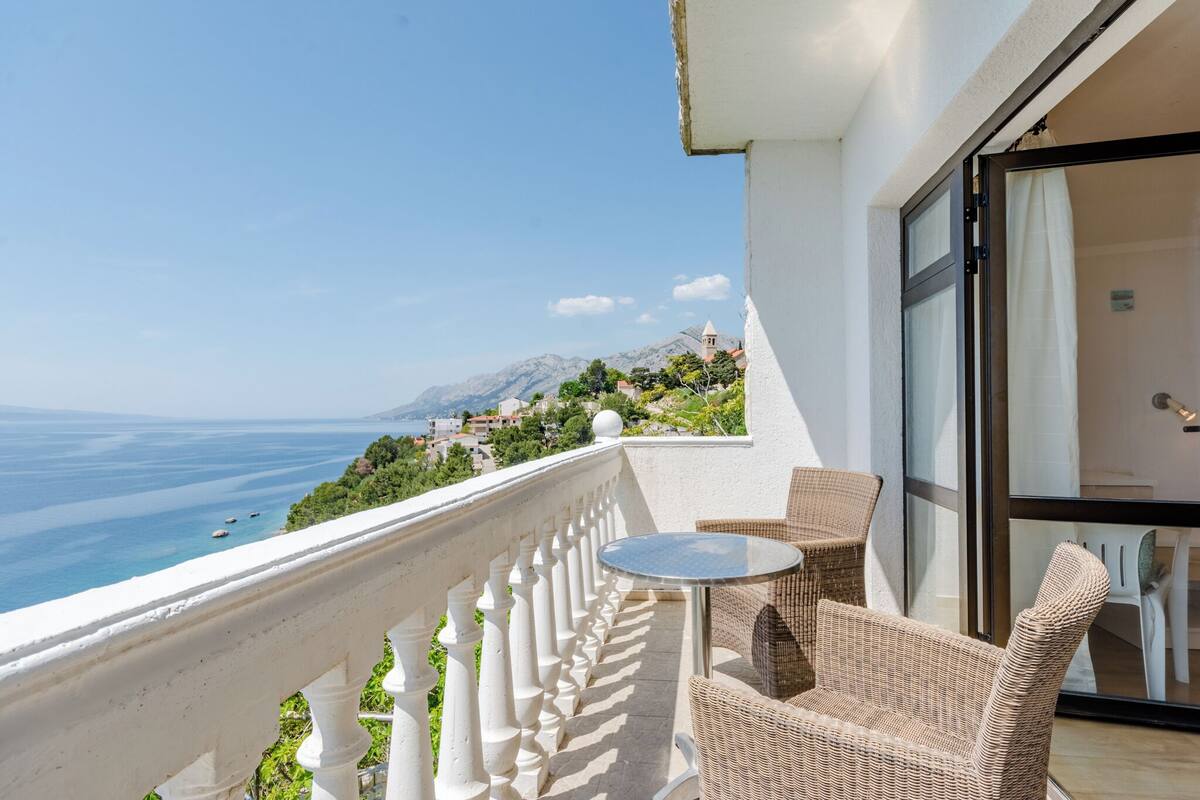 A balcony with wicker furniture, a glass door, and a view of the sea and mountains.