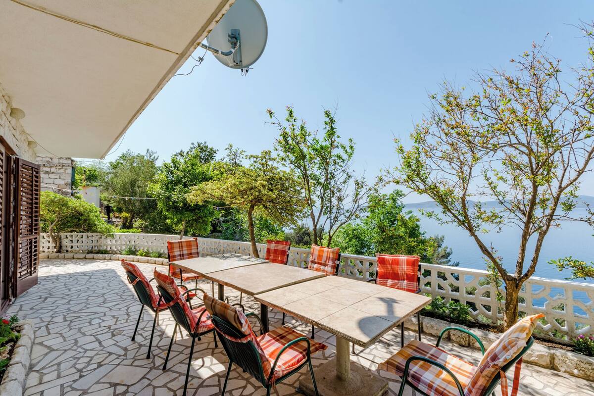 An outdoor patio with a table and chairs, a satellite dish, and a view of the sea.