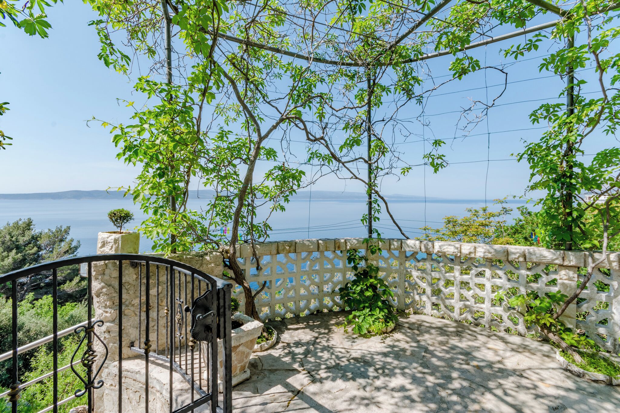 A balcony with a stone railing, a view of the sea, and a lattice fence.