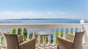 A balcony with wicker furniture and a small table, overlooking a scenic view of the sea and distant land. - Villa Kosa (Brela)