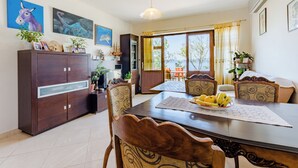 A dining area with a wooden table, chairs, and a cabinet. There are paintings on the wall and a window with curtains. - Villa Kosa (Brela)