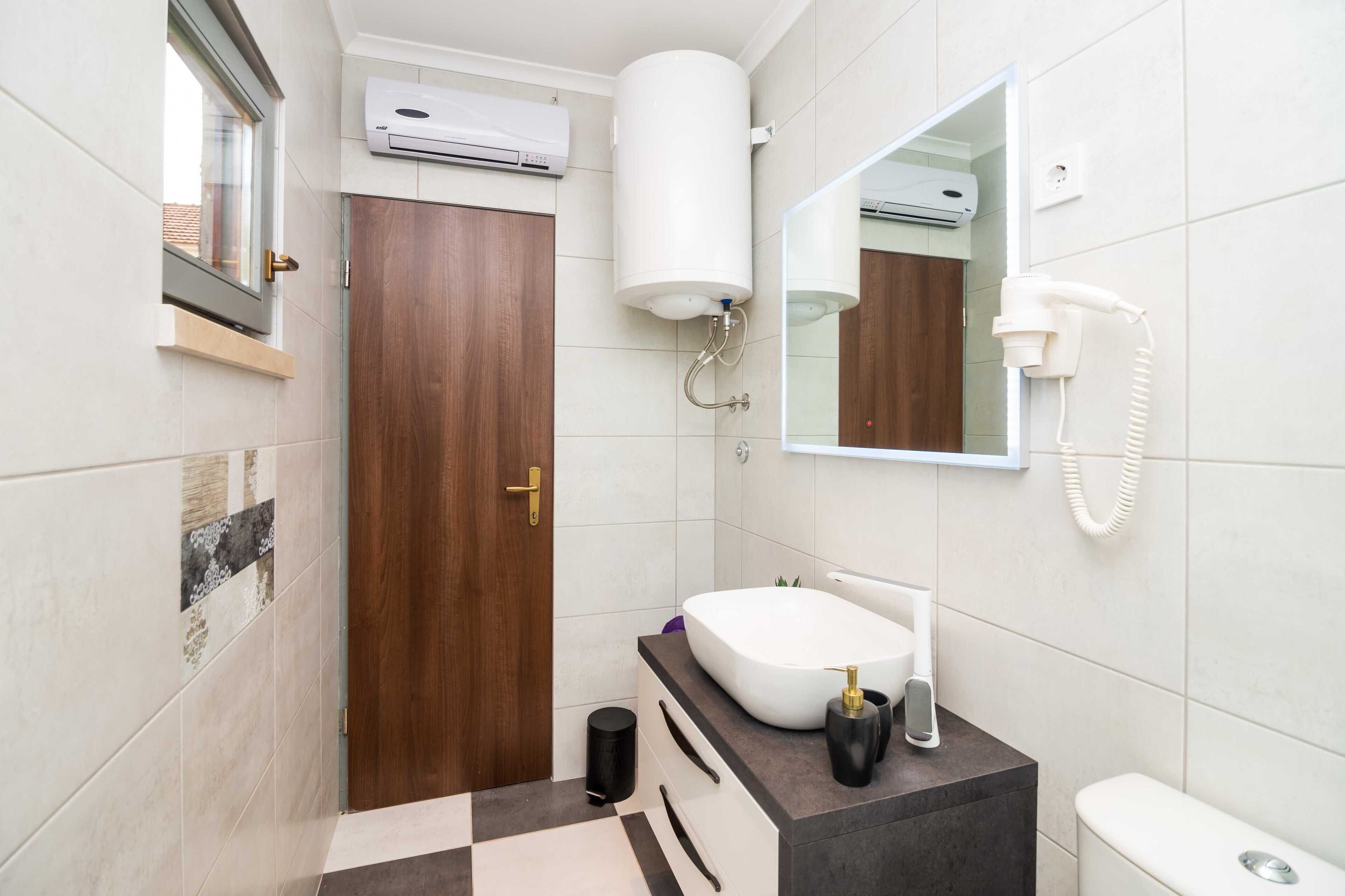 Un baño moderno con puerta de madera, lavamanos blanco, espejo y retrete.