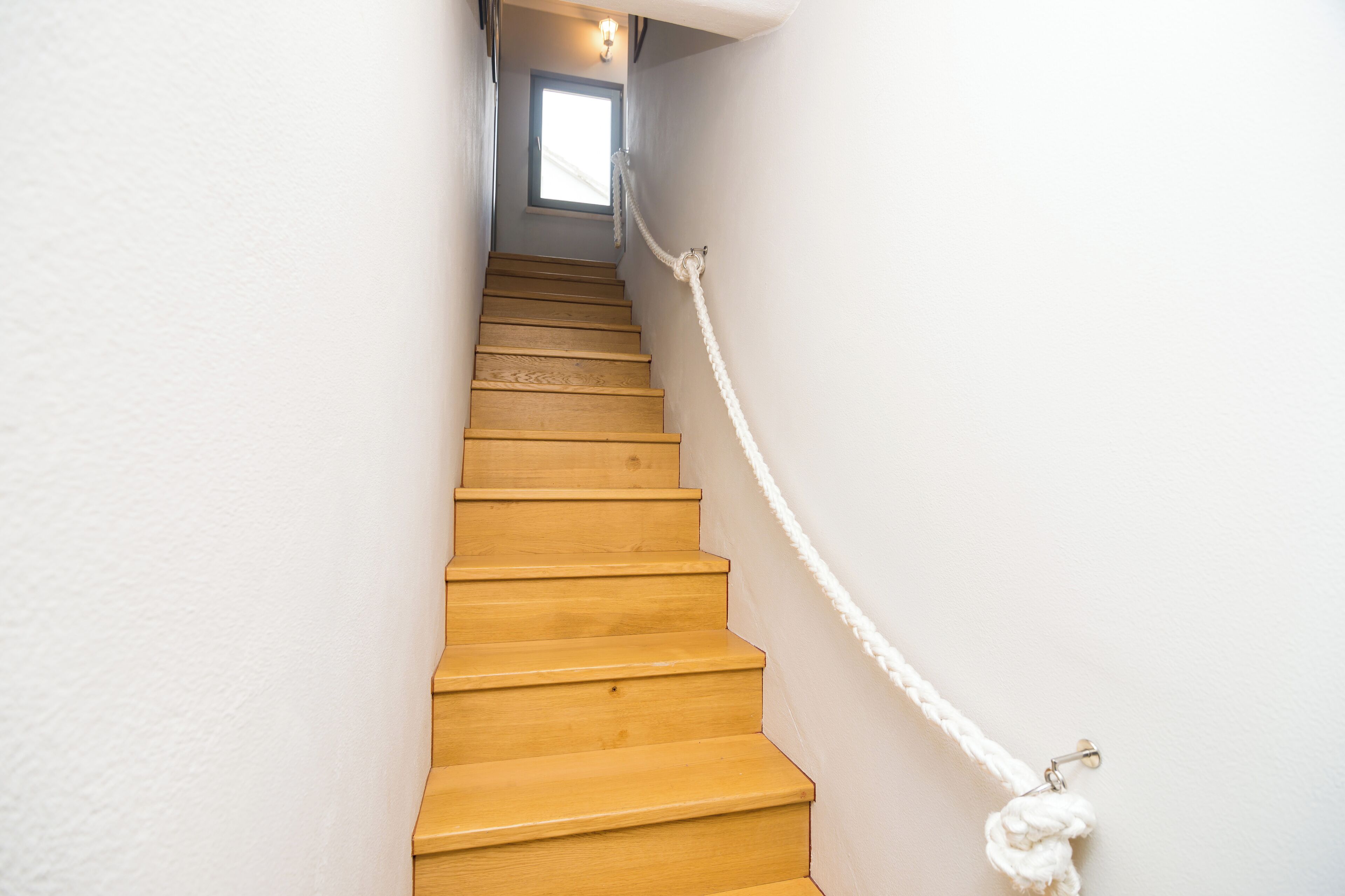 A wooden staircase with a rope barrier, leading to a room with a window.