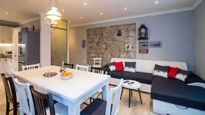 A modern kitchen with white cabinets, a stone wall, and a dining area with a white table and chairs. - Villa Nives (Ston)
