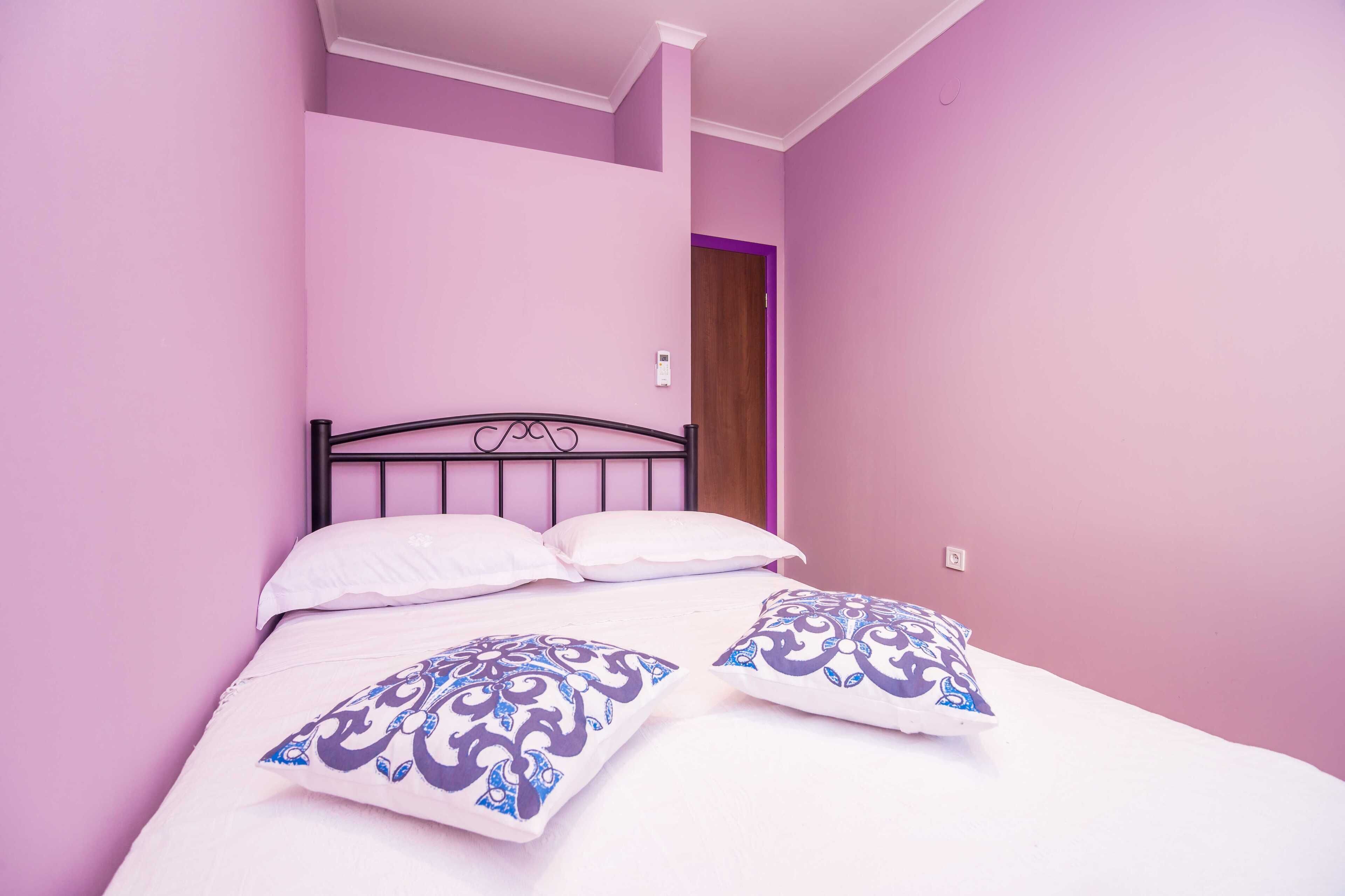Una cama individual con estructura metálica, ropa de cama blanca y dos almohadones decorativos.
