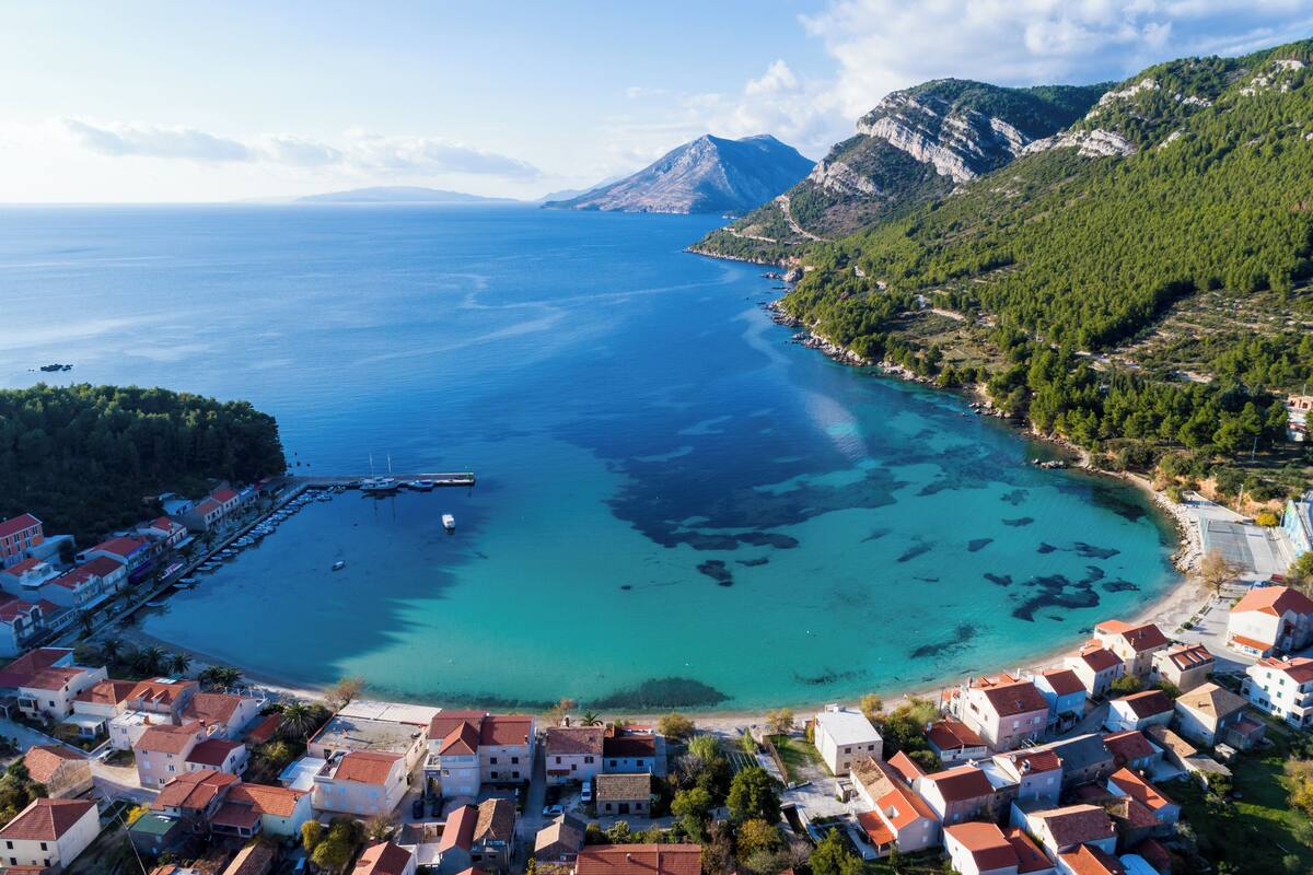 A coastal town with a marina, clear turquoise waters, and mountainous backdrop.