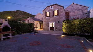 A stone building with a wooden door and windows, surrounded by a paved area with hexagonal tiles. - Villa Nives (Ston)