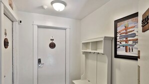 A hallway with a white door marked 523, a coat rack, and a framed sign with ski area names. - Renovated Killington Center Studio. Close to Resort. Bus. Discounted Ski Rentals. 523 (Killington)