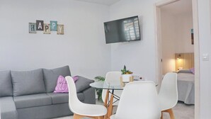Moderni olohuone, jossa on harmaa sohva, valkoiset tuolit, lasinen sohvapöytä ja seinälle asennettu litteänäyttöinen televisio.