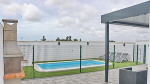 Kattoterassilla sijaitseva uima-allas, jossa on verkkoaita, aurinkotuoleja ja pergola.