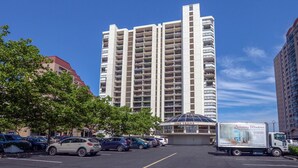 Et højt, moderne hotel med flere etager og balkoner, en parkeringsplads med flere biler og en varevogn foran.