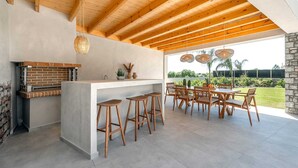 An outdoor kitchen with a brick oven, wooden stools, and a dining table with chairs. - Welcome to Emerald Estate, your serene retreat on Rhodes Island. (Rhodes)