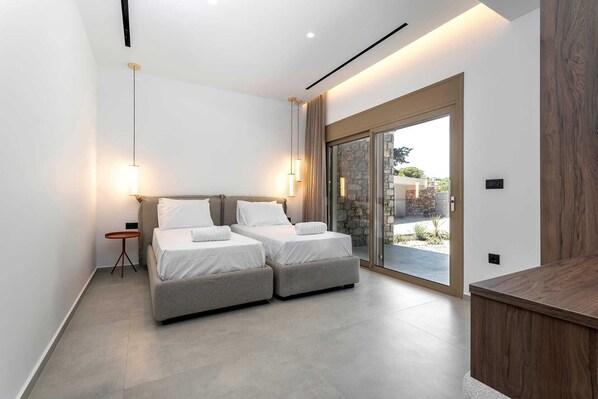 A modern bedroom with two beds, a small side table, and a large sliding glass door leading to an outdoor area.