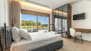 A modern bedroom with a bed, a TV, a desk, and a view of a pool. - Welcome to Emerald Estate, your serene retreat on Rhodes Island. (Rhodes)