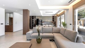 A modern living room with a sectional sofa, a coffee table, and a kitchen in the background. - Welcome to Emerald Estate, your serene retreat on Rhodes Island. (Rhodes)