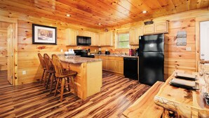 A wooden cabin interior with a kitchen featuring wooden cabinets, a black refrigerator, and a dining area with wooden chairs and a table. - 2BR, sleeps up to 10, less than 8 minutes to Dollywood, Island, Parkway! (Pigeon Forge)