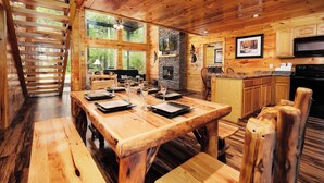 A wooden interior with a dining table set for four, a stone fireplace, wooden cabinets, and large windows. - 2BR, sleeps up to 10, less than 8 minutes to Dollywood, Island, Parkway! (Pigeon Forge)