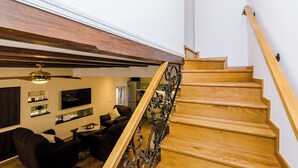 A wooden staircase with a metal railing leading to a living area with a sofa, TV, and shelves.