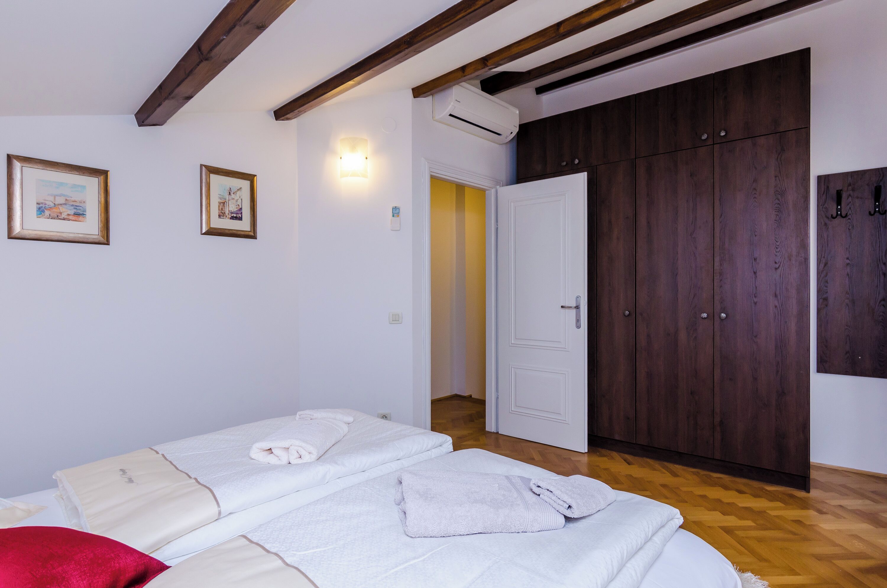 A bedroom with two beds, a wooden wardrobe, and a door leading to another room.