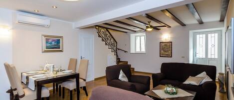 Comedor con una mesa de madera dispuesta para cuatro personas, una escalera y un área de estar con dos sofás.