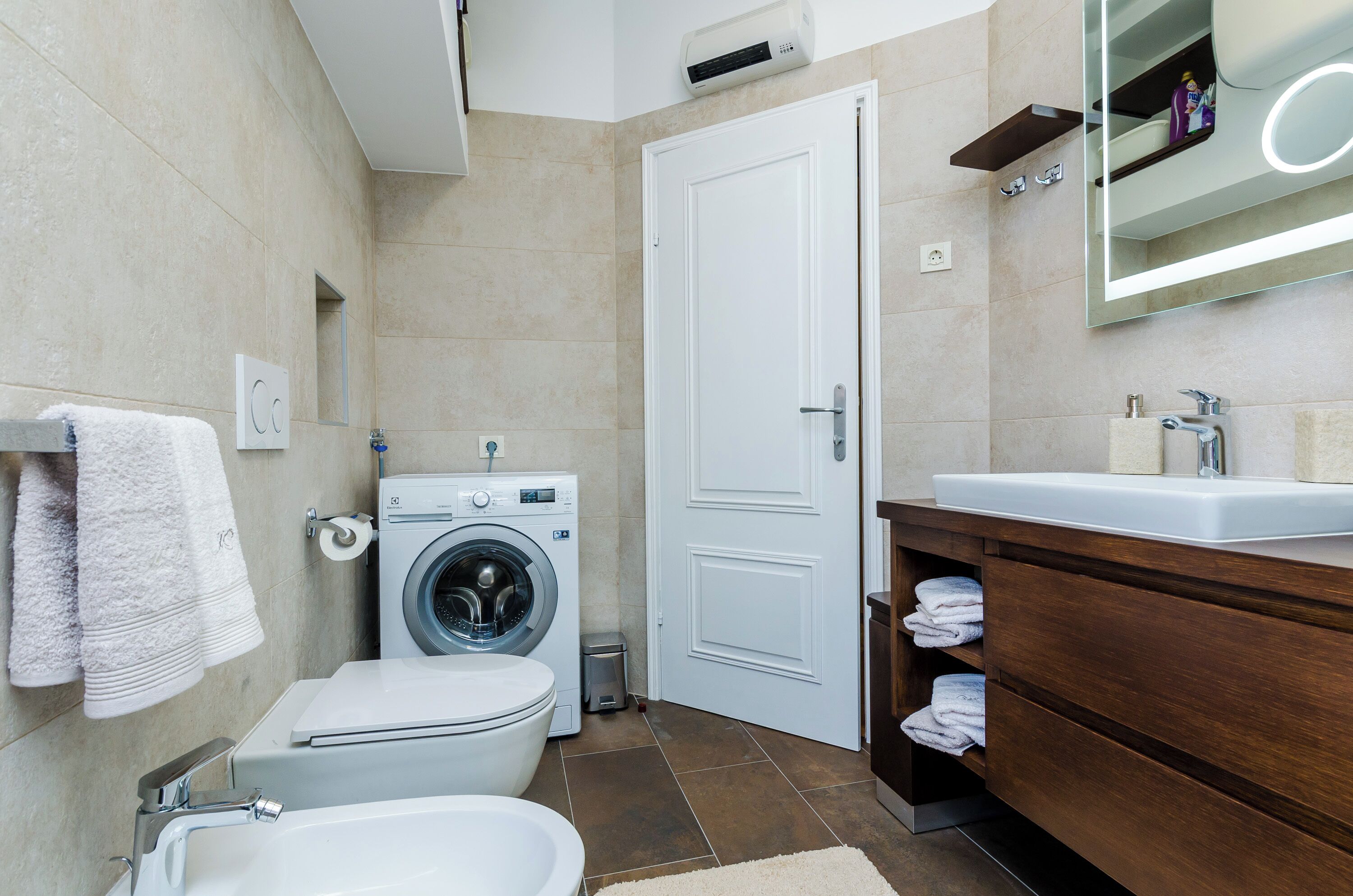 A modern bathroom with a washing machine, toilet, and sink.