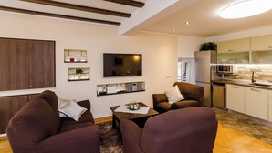 A modern living room with a sofa, coffee table, and a flat-screen TV. There is a kitchen area with a microwave and refrigerator.