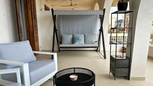 Une pièce comprenant un canapé, un fauteuil suspendu, une table ronde et une étagère en métal.