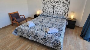 A neatly made bed with a patterned bedspread, two bedside tables with lamps, a chair, and a wooden floor. - Jardines Canarios 1 - Three Bed (Los Cristianos)