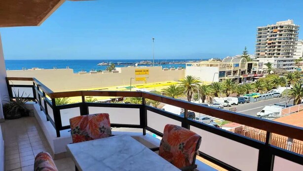 A balcony with a table and chairs, overlooking a beach and a cityscape. - Jardines Canarios 1 - Three Bed (Los Cristianos)