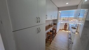 A modern kitchen with white cabinets, wooden stools, and a view through the window. - Jardines Canarios 1 - Three Bed (Los Cristianos)