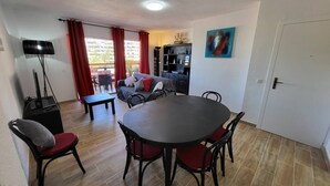 A dining area with a round table and chairs, a sofa, a TV, and a bookshelf. - Jardines Canarios 1 - Three Bed (Los Cristianos)