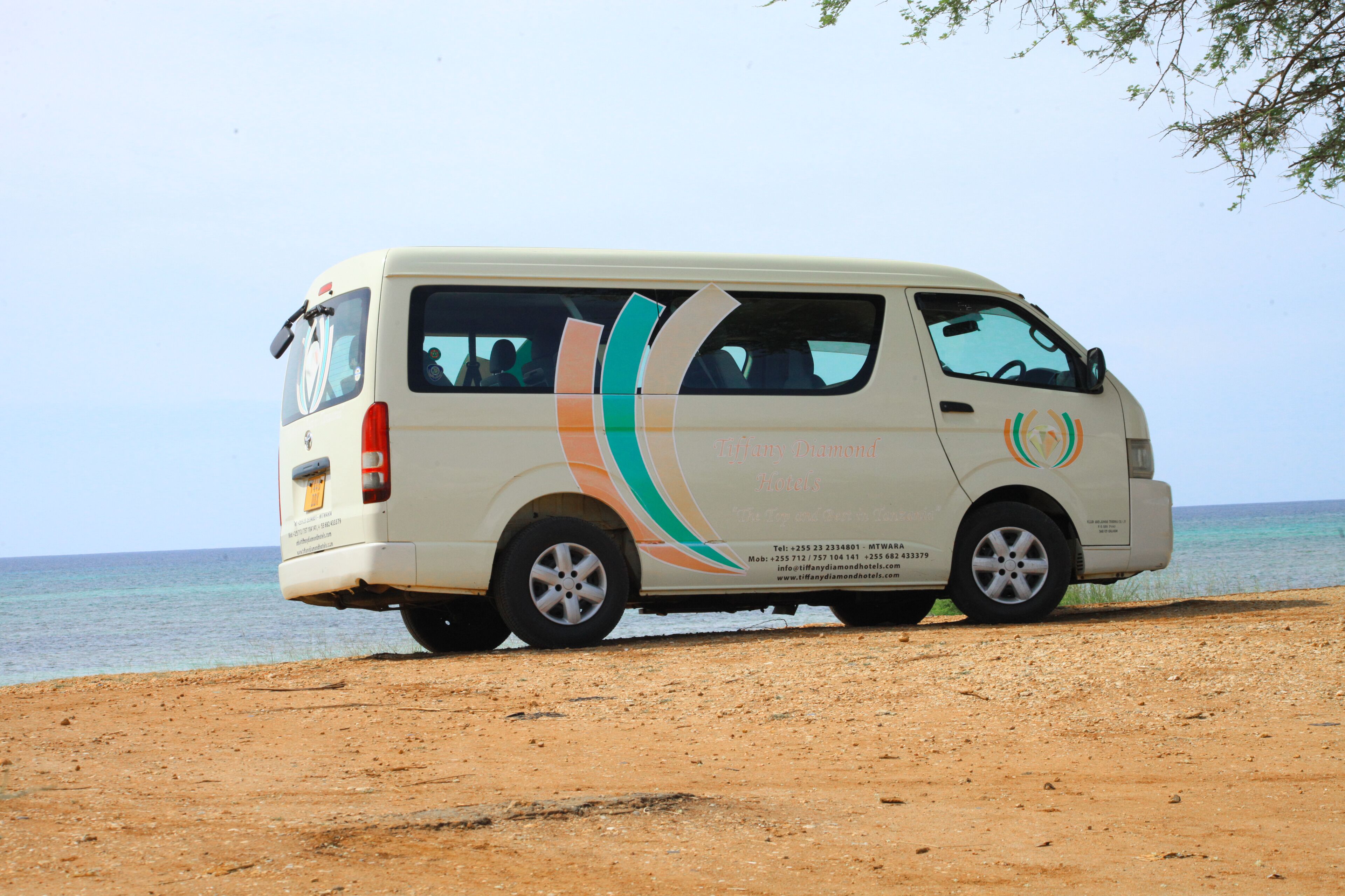 A van parked on a sandy beach with a clear view of the ocean in the background.