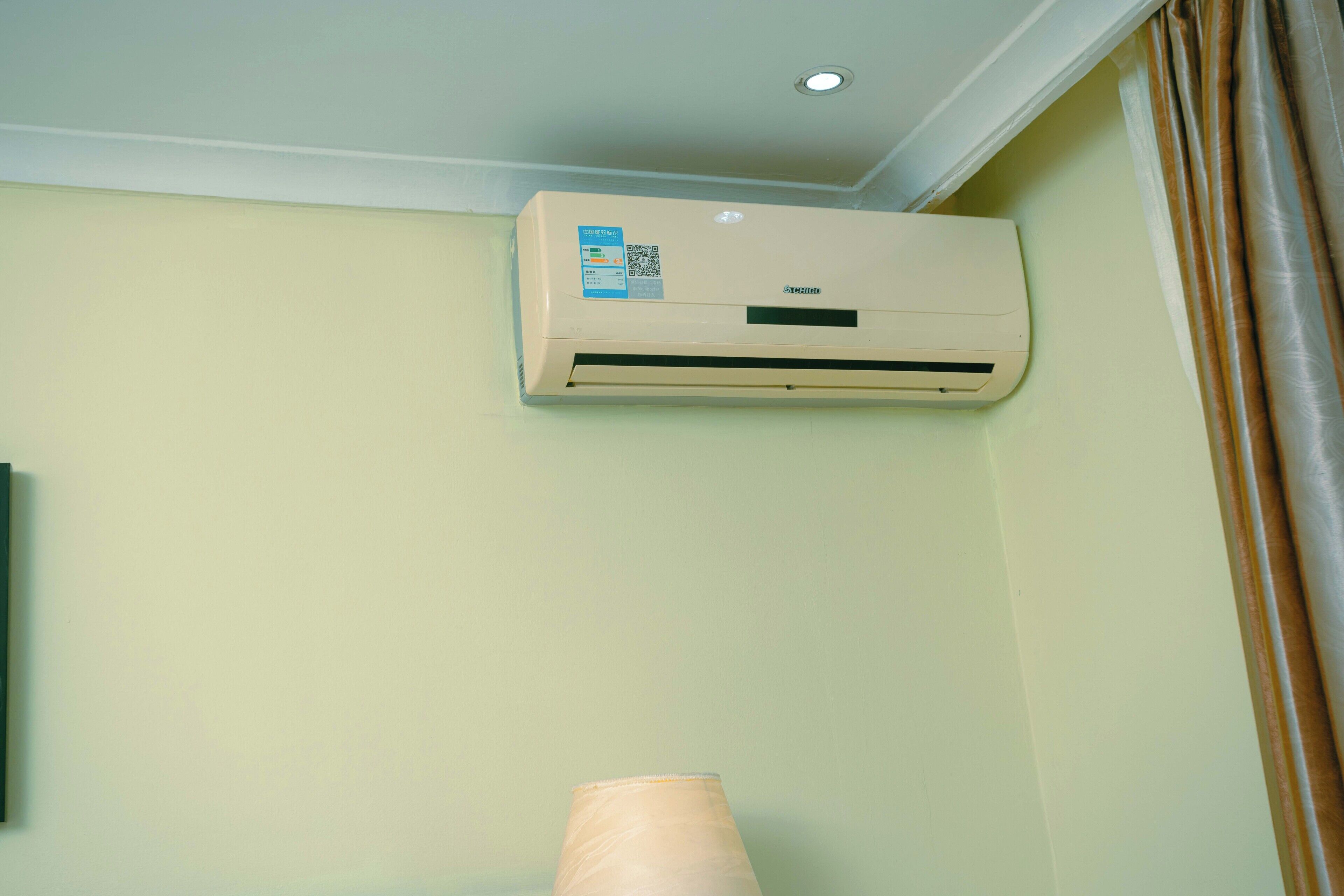 Eine Wand-Klimaanlage in einem Raum mit schlichter Wandgestaltung und einem Vorhang auf der rechten Seite.