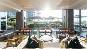 A modern outdoor seating area with tables and chairs, large umbrellas, and a view of a cityscape. - Luxury Apartment Sandton / no Loadshedding / Dstv (Johannesburg)