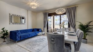 Una sala moderna con un sofá azul, una mesa de comedor para cuatro personas y un espejo grande en la pared.